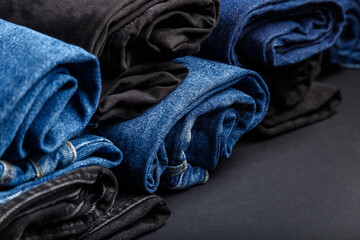 Blue jeans folded in rolls lie on black background. Black and blue denim pants in form of rolls....