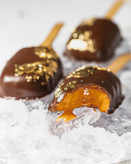 Popsicles, covered with chocolate, with a leaf of edible gold on top on an icy background with snow. Popsicle and sweet dessert on a stick.