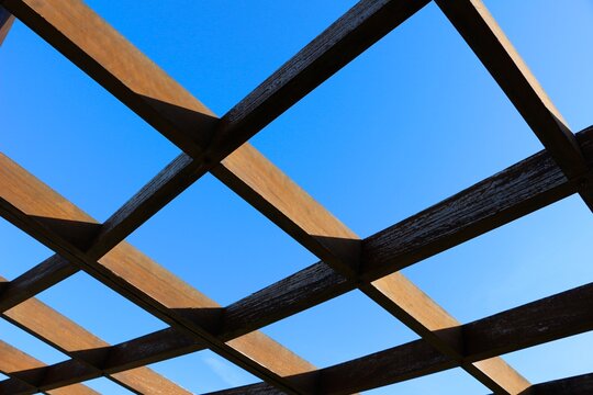 Looking up through a lattice wooden grid with a clear blue sky on a sunny morning