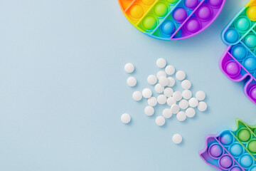Sensory toy Poppit and pills on blue background as medication for ADHD or autism. Colorful silicone bubbles and a bunch of tablets for stress and anxiety relief with copy space