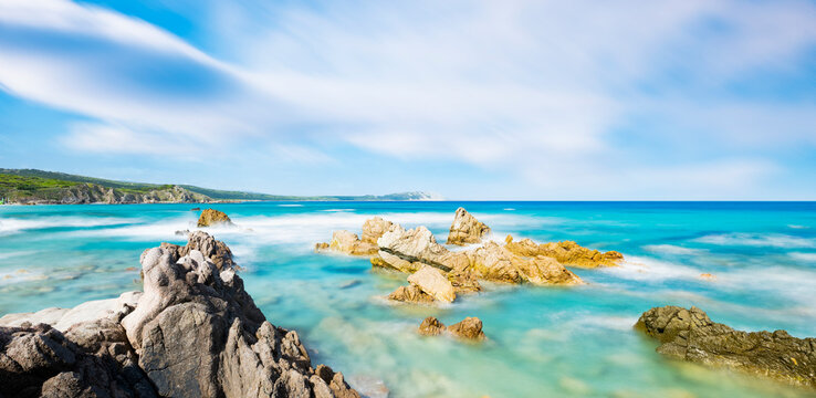 (Long exposure) Stunning view of a rocky coastline bathed by a turquoise, clear sea during a sunny, summer day, Rena Majore, Sardinia, Italy.