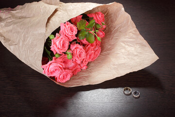 Bouquet of roses in a crumpled paper package and wedding rings