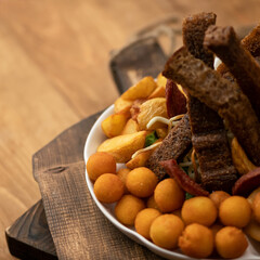 Beer snack. Close up of potato croquettes, black bread croutons and fried potatoes on blurred...