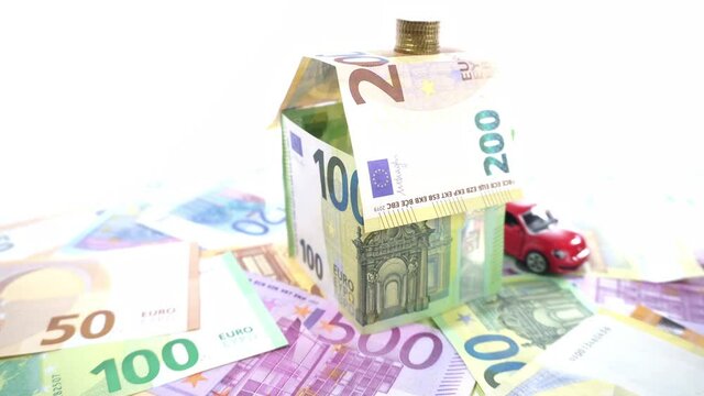 Haus aus Geldscheinen mit Auto - Hauskredit Symbolbild