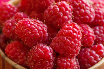 Ripe raspberries in a wooden container on a red background. Close up