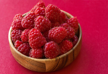 Ripe raspberries in a wooden container on a red background.