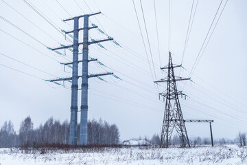 High voltage power line towers in a winter climate. It can be seen snowing. Snowy field and forest line on background