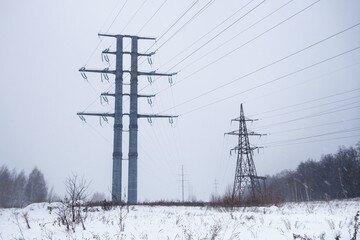 Line of high voltage power transmission towers. Winter, you can see how it is snowing. Snowy field and forest on the background