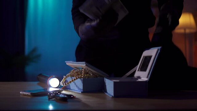 Robber in a balaclava steals jewelry and money from a table