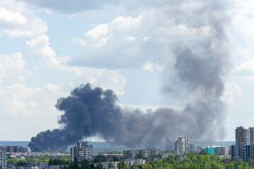 Fire in the city. Black column of smoke rises to the sky over city buildings