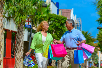 Happy senior couple holding colorful shopping bags outdoors walking in the city 