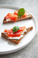 Bruschetta with red fish and cream cheese with black bread on white plate.
