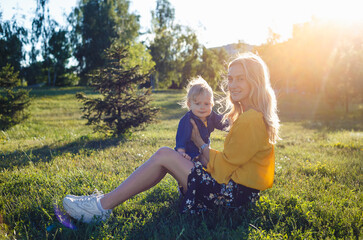 Beautiful young woman with boy on the daisy meadow on a sunny day. Happy family on summer sunset. Mum with baby.