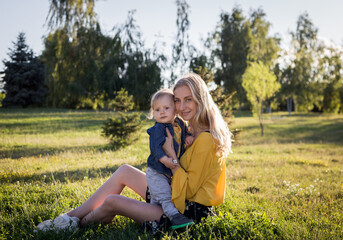 Beautiful young woman with boy on the daisy meadow on a sunny day. Happy family on summer sunset. Mum with baby.