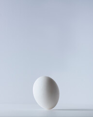 White egg tiling on its tip about ready to fall against a white background.