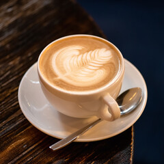Coffee with milk. Cappuccino with creamy foam. Rest break from business with natural energy drink. Foam drawing. Cup of aromatic coffee with spoon and saucer on a dark background.
