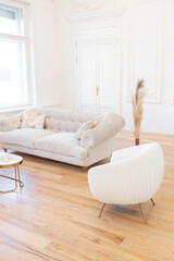 very light baroque style luxury interior of big sitting room. White walls decorated with awesome stucco. Royal style apartment with chic furniture with gold elements