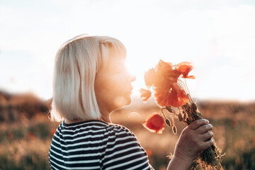 Happy blonde hair woman holding red poppies bouquet in the field at sunset at sunset