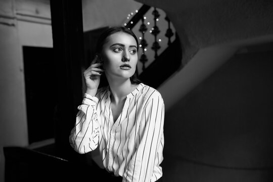 Black and white indoor portrait of a sad charming young woman wears striped white shirt