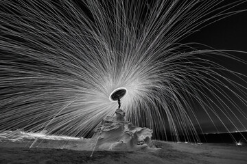 Photographie de laine d& 39 acier à la structure rocheuse du désert la nuit avec des éclaboussures de feu partout. Photographie à vitesse d& 39 obturation lente avec de la laine d& 39 acier en noir et blanc
