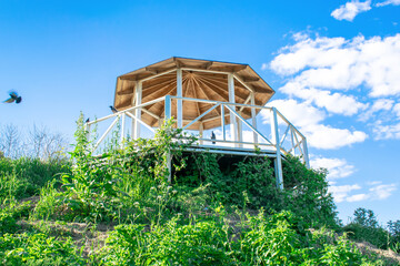 Beautiful wooden carved open alcove, arbor in city botanic park in spring summer sunny day against blue sky with bright sunlight