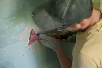 Caucasian man removing old paint with scraper tool.