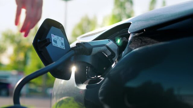 Man Plugging In Charger Into An Electric Car At Charge Station. Slow Motion