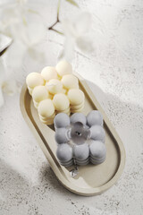 Two grey-blue and white bubble candles on a concrete tray on pastel background, a close up