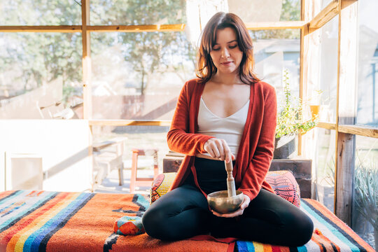 Woman meditating and playing brass singing bowl