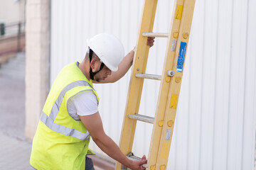 telecommunications technician with safety helmet and reflective vest, deploying a yellow ladder while looking down.
