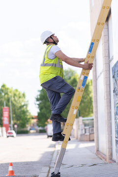 telecommunications technician climbing a yellow ladder wearing reflective vest, boots and safety helmet 