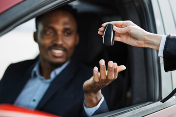Female auto seller giving keys to male customer form his new electric car. Handsome african man in...