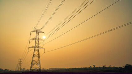 High power electricity pole silhouetted against the orange sky at dusk, Electric pole in India,...