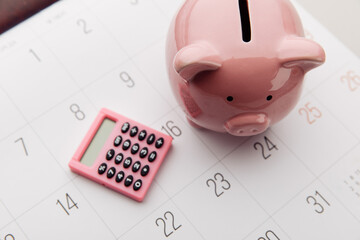 Pink piggy bank and calculator on a white calendar background, saving and investment concept. Top...