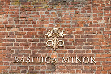 The Basilica Minor sign on the red bricks wall at the entrance to the church. In recent times, the title of minor basilica has been attributed to important pilgrimage churches. 