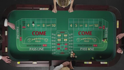 Top view of two men and a woman playing craps while sitting at a table in a casino. Players place bets with chips. The man throws the dice and wins. Slow motion ready, 4K at 59.94fps.