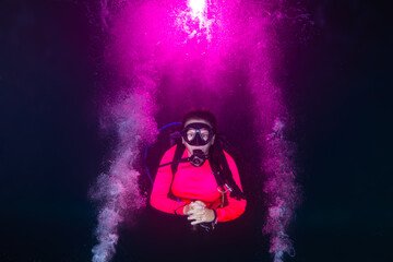 A female scuba diver relaxes into a night dive as explosions of pink bubbles decorate the water...