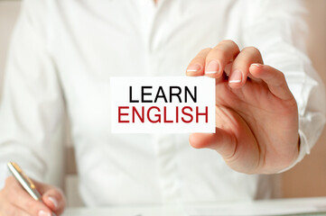 a woman in a white shirt holds a piece of paper with the text: learn english. business concept.