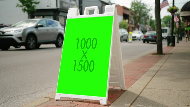A view of a green screen sandwich board on the sidewalk of a small town's main street. Promote business or sales.  	