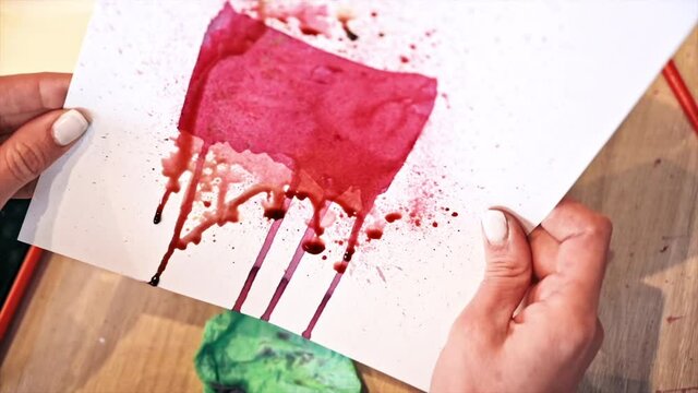 A woman in a studio painting on paper with red wine and wipe, close view, slow motion