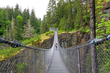 Vancouver Island - Elk Falls Provincial Park suspension bridge. The view on the hiker walking on the bridge above deep canyon. - obrazy, fototapety, plakaty