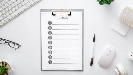 Goals list on workspace on white background. Flat lay, top view office table desk. New ideas on home work space with keyboard mouse glasses papers plants laptop. Long web banner