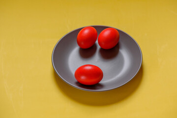 Red eggs, yellow background. Three eggs in a gray plate on a yellow background.