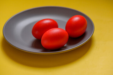 Red eggs, yellow background. Three eggs in a gray plate on a yellow background.