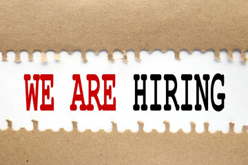 WE'RE HIRING Concept. text on torn cardboard. black letters on white paper