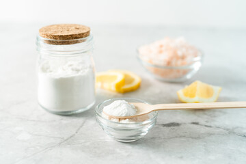 Eco friendly natural cleaners, jar with baking soda, lemon, pink salt and wooden spoon on marble table background. Organic ingredients for homemade cleaning. Zero waste concept.