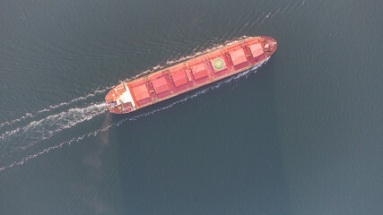 A large ocean-going cargo ship moves out to sea on calm waters. Dry cargo ship aerial view.