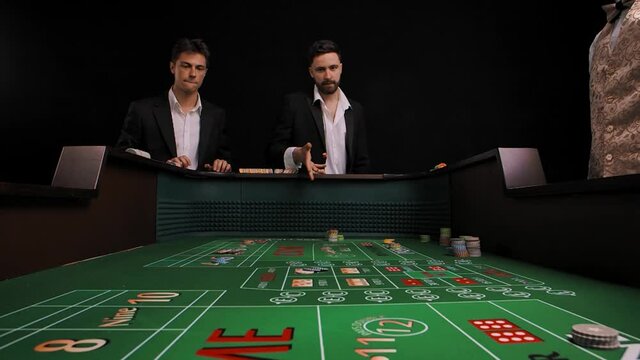 Two men in business suits stand at a green craps table in a casino. The player rolls the dice and loses. The males are very upset and disappointed. View from inside of game table. Slow motion.