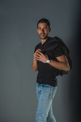 Strong muscular male model in jeans with black t-shirt holding his jacket over his shoulders