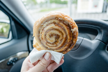 Man passing time waiting in car eating a cinnamon roll